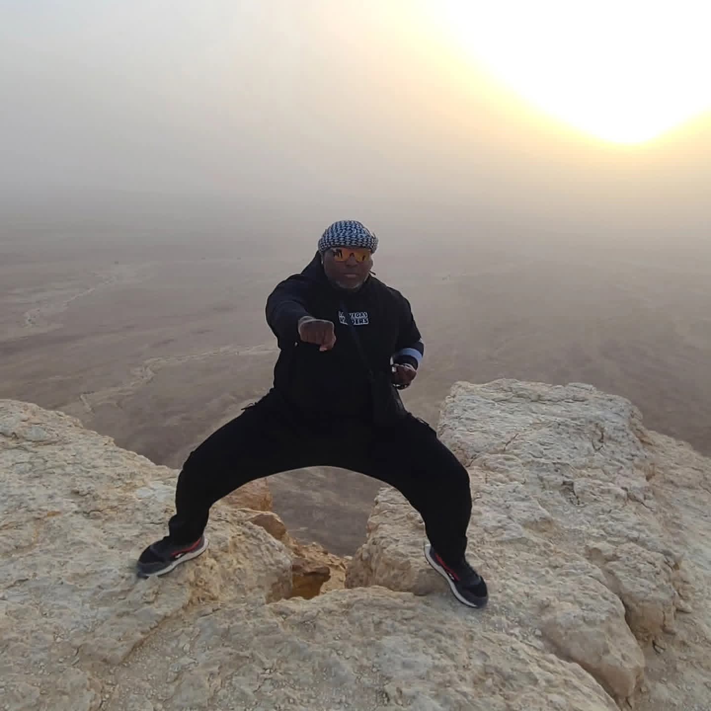 Coach in a wide power stance on a cliff edge at sunrise — Edge of the World, Saudi Arabia